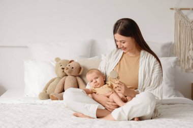 Çıngıraklı mutlu anne ve küçük bebeği yatak odasında oturuyor.