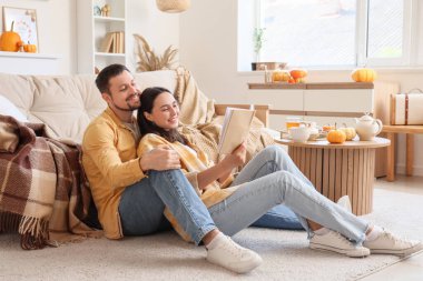 Mutlu genç çift güz günü evde kitap okuyor.