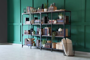 Yastıklı sepet ve içinde yeşil duvarın yanındaki kitapların olduğu raf ünitesi.