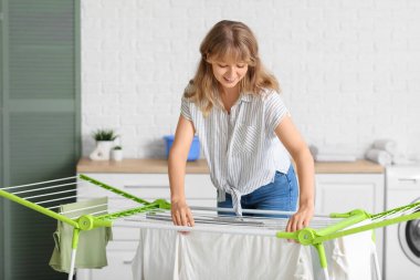 Genç bir kadın evdeki kurutucuya temiz çamaşır asıyor.