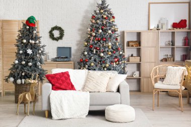 Noel için dekore edilmiş oturma odasının içi kanepe, raf ünitesi ve beyaz tuğla duvarın yanındaki şifoniyerle süslenmiş.