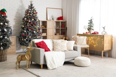 Noel için dekore edilmiş oturma odasının içi kanepe, raf ünitesi ve beyaz tuğla duvarın yanındaki şifoniyerle süslenmiş.