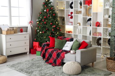 Oturma odasının içi Noel için dekore edilmiş kanepe, raf ünitesi ve pencerenin yanındaki şifoniyerle.