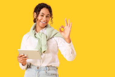 Tablet bilgisayarlı genç Afro-Amerikan soru cevap mühendisi sarı arka planda iyi görünüyor.