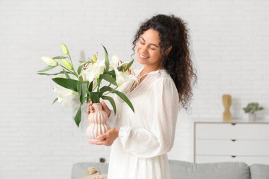 Güzel, mutlu, Afro-Amerikalı bir kadın elinde bir buket beyaz zambak çiçeğiyle evde.