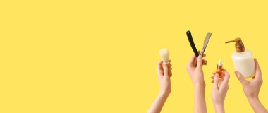 Eller düz jilet, tıraş fırçası ve sarı arkaplandaki kozmetik ürünlerini tutuyor.