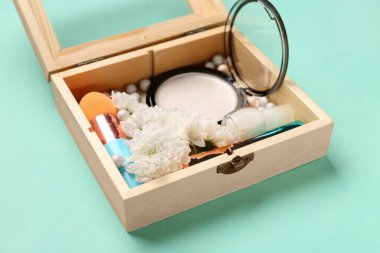 Makyaj ürünleri ve turkuaz arka planda güzel kasımpatı çiçekleri olan ahşap kutu, yakın plan.