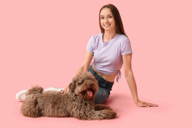 Pembe arka planda oturan sevimli kahverengi kaniş köpekli genç bir kadın.