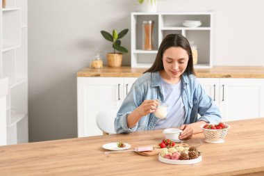 Güzel genç bayan mutfakta çikolata kaplı çilek hazırlıyor.