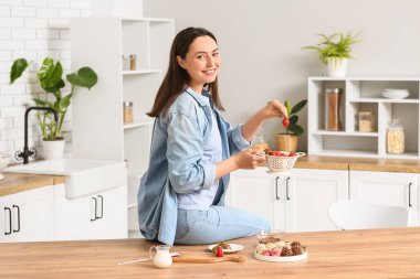 Güzel genç bayan mutfakta çikolata kaplı çilek hazırlıyor.