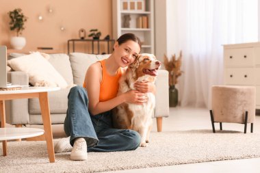 Genç bir kadın, oturma odasında yerde tatlı bir Avustralya çoban köpeğine sarılıyor.