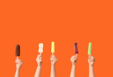 Turuncu arka planda farklı tatlı dondurmalı kadın elleri.