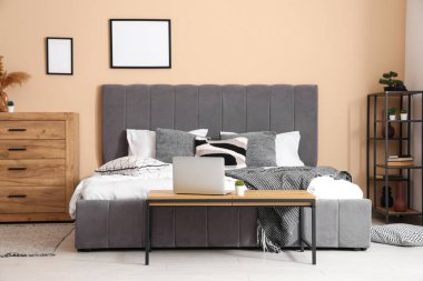 Rahat yataklı şık bir oda, dizüstü bilgisayarlı bank, çekmeceler ve raf ünitesi.