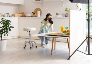 Profesyonel ekipmanlarla genç bayan yemek fotoğrafçısı modern mutfakta kokteyllerin fotoğrafını çekiyor.