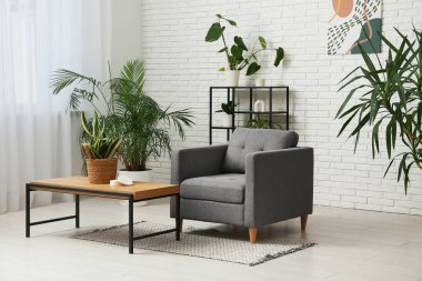 Oturma odasının iç tarafındaki beyaz tuğla duvarın yanında rahat bir koltuk, masa ve bitkiler.