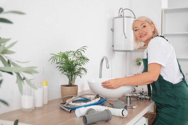 Olgun kadın tesisatçı lavaboyu banyoya yerleştiriyor.