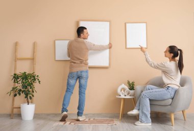 Genç kadın ve kocası evdeki bej duvarda boş bir çerçeve asılı.