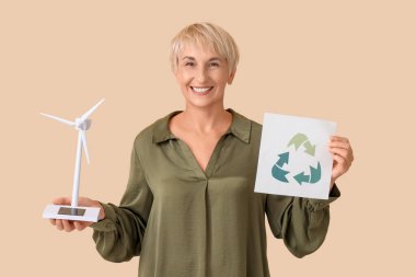 Rüzgâr türbini modeli ve bej arka planda geri dönüşüm işareti olan olgun bir kadın