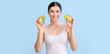 Açık mavi arka planda avokadosu olan güzel genç bir kadın.