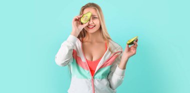 Turkuaz arka planda avokado yapan genç bir kadın.