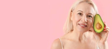 Pembe arka planda taze avokado tutan olgun bir kadın. 