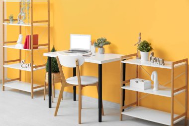 Masası, modern dizüstü bilgisayarı ve raf ünitesi olan hafif bir ofis.