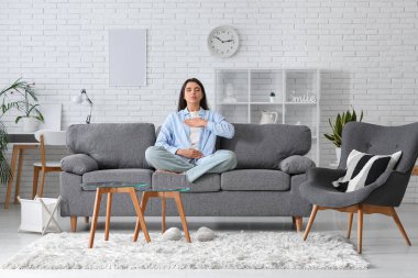 Beautiful young woman doing breath practice on sofa at home