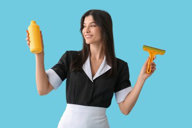 Mavi arka planda cam sileceği ve deterjanı olan genç oda hizmetçisi.