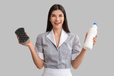 Temizlik süngeri ve hafif arka planda deterjanı olan genç oda hizmetçisi.