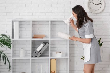 Genç oda hizmetçisi ofisinde toz bezi ile rafı temizliyor.