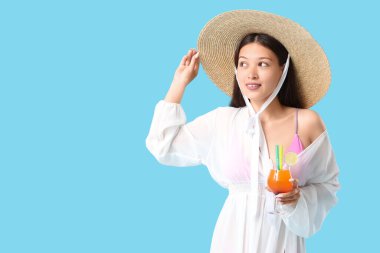 Mavi arka planda bir bardak kokteyl ile güzel bir Asyalı kadın.