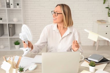 Elektrikli vantilatör ve dizüstü bilgisayarı olan olgun bir iş kadını.