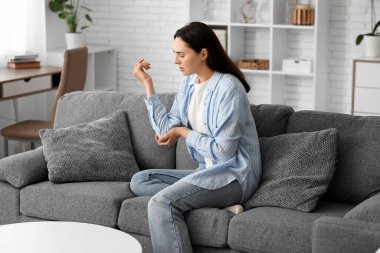 Evdeki kanepede dirsek ağrısı çeken genç bir kadın.