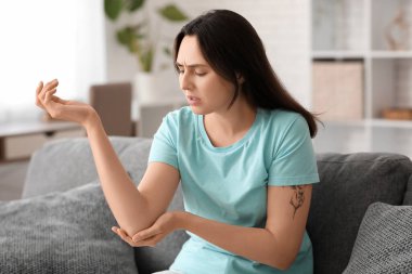Evdeki kanepede dirsek ağrısı çeken genç bir kadın.