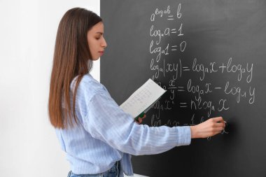 Sınıfta yazı tahtasının yanında genç bayan matematik öğretmeni.