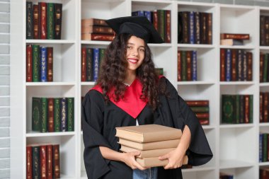 Kütüphanenin kitap raflarının yanında yığınla kitabı olan mezun bir bayan öğrenci.