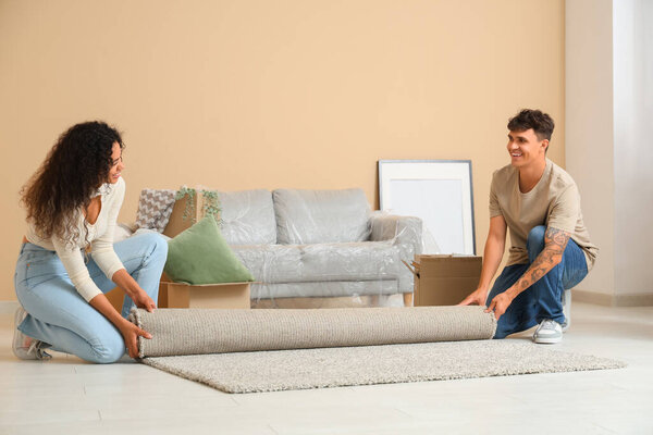 Young couple placing carpet near cardboard boxes with belongings in their new flat