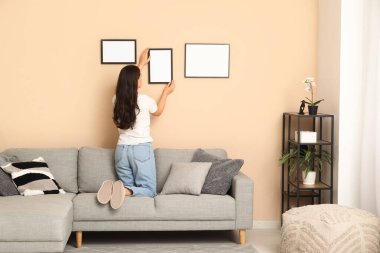 Evdeki bej duvarda boş bir çerçeve asılı genç bir kadın. Arka plan