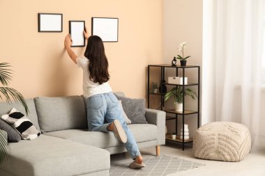 Evdeki bej duvarda boş bir çerçeve asılı genç bir kadın. Arka plan