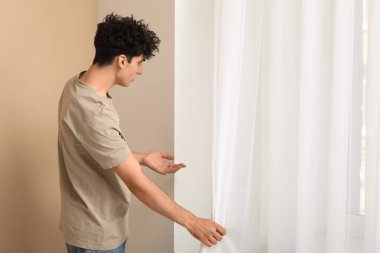 Evinin penceresinin yanındaki duvarda küf olan genç adam.