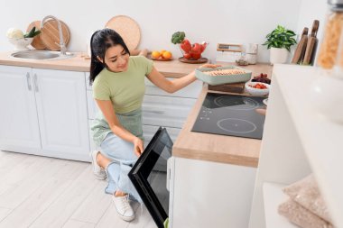 Genç bir kadın elmalı turtayla pişirme tabağını mutfakta elektrikli fırına koyuyor.