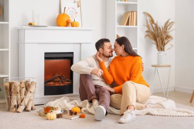 Sonbahar dekoru olan mutlu genç çift şöminenin yanında oturuyor.