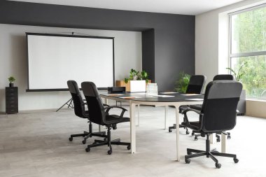 Masa ve projektör ekranlı konferans salonunun içi