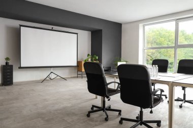 Masa ve projektör ekranlı konferans salonunun içi