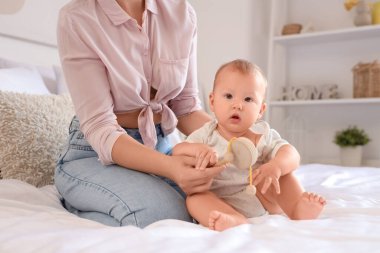 Güzel, genç bir anne ve yatak odasında çıngıraklı küçük sevimli bir bebek oturuyor.