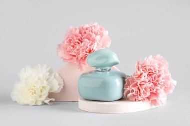 Bir şişe parfüm, alçı tezgahları ve beyaz arka planda karanfiller.