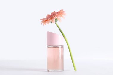 Beyaz arka planda bir şişe parfüm ve gerbera çiçeği.