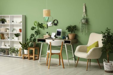 Tabletli, raflı ve evdeki yeşil duvarın yanındaki farklı evlerden oluşan şık bir iş yeri.