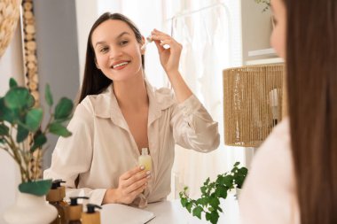 Makyaj odasında aynanın yanında serum uygulayan genç bir kadın.