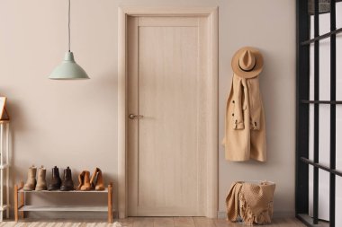 Beyaz duvarda asılı ayakkabı standı, kapısı ve ceketi olan şık bir koridorun içinde.